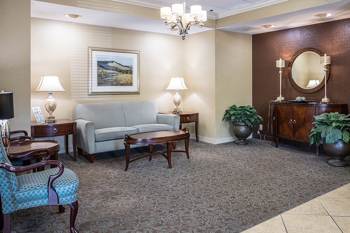 Lobby with chandelier, sofa, chair, tables, lamps and round mirror
