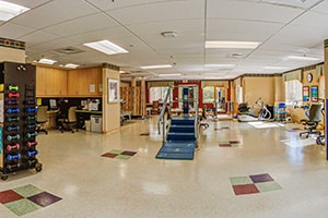 Rehab gym with physical therapy equipment and many large windows.