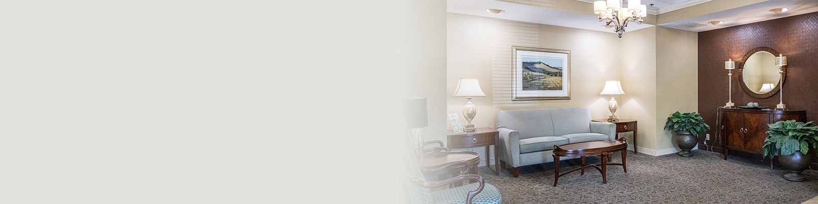 Lobby with chandelier, sofa, chair, tables, lamps and round mirror